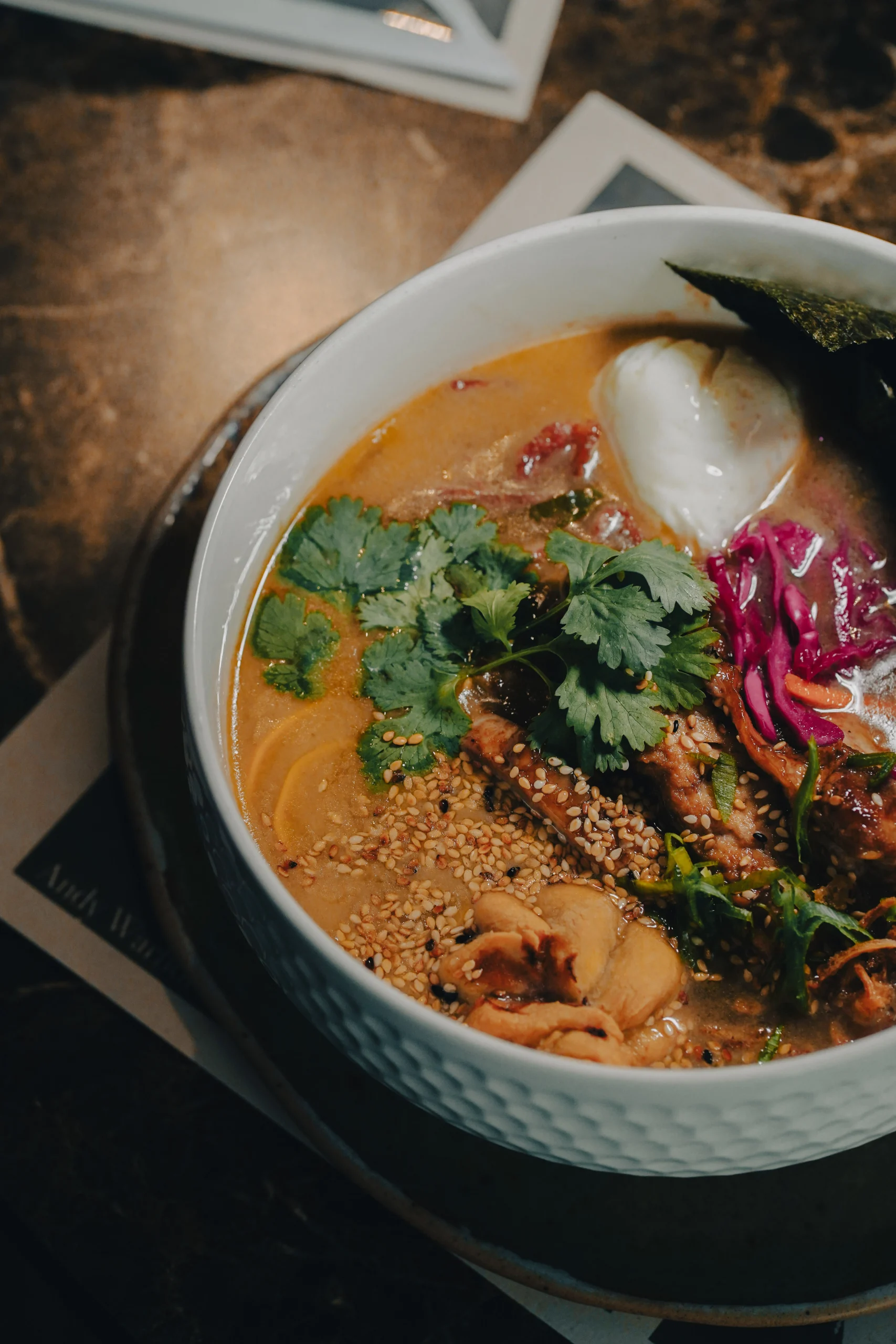 Bowl de ramen con caldo dorado, huevo tibio, carne, nori, repollo encurtido y cilantro fresco – fotografía gastronómica con contraste de texturas por Suma Estudios