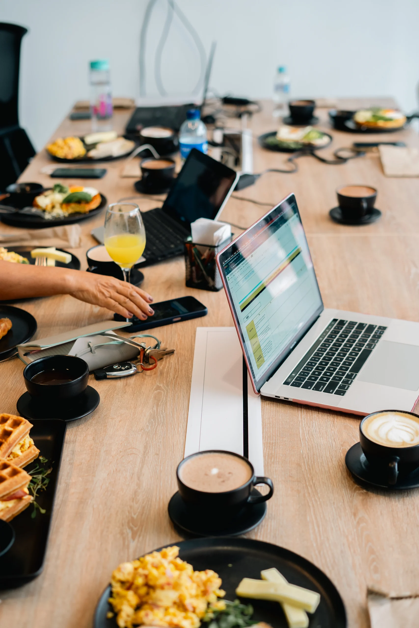 Mesa de trabajo con laptops y desayuno compartido – huevos, waffles, café y jugo durante reunión de equipo – fotografía documental de ambiente colaborativo por Suma Estudios
