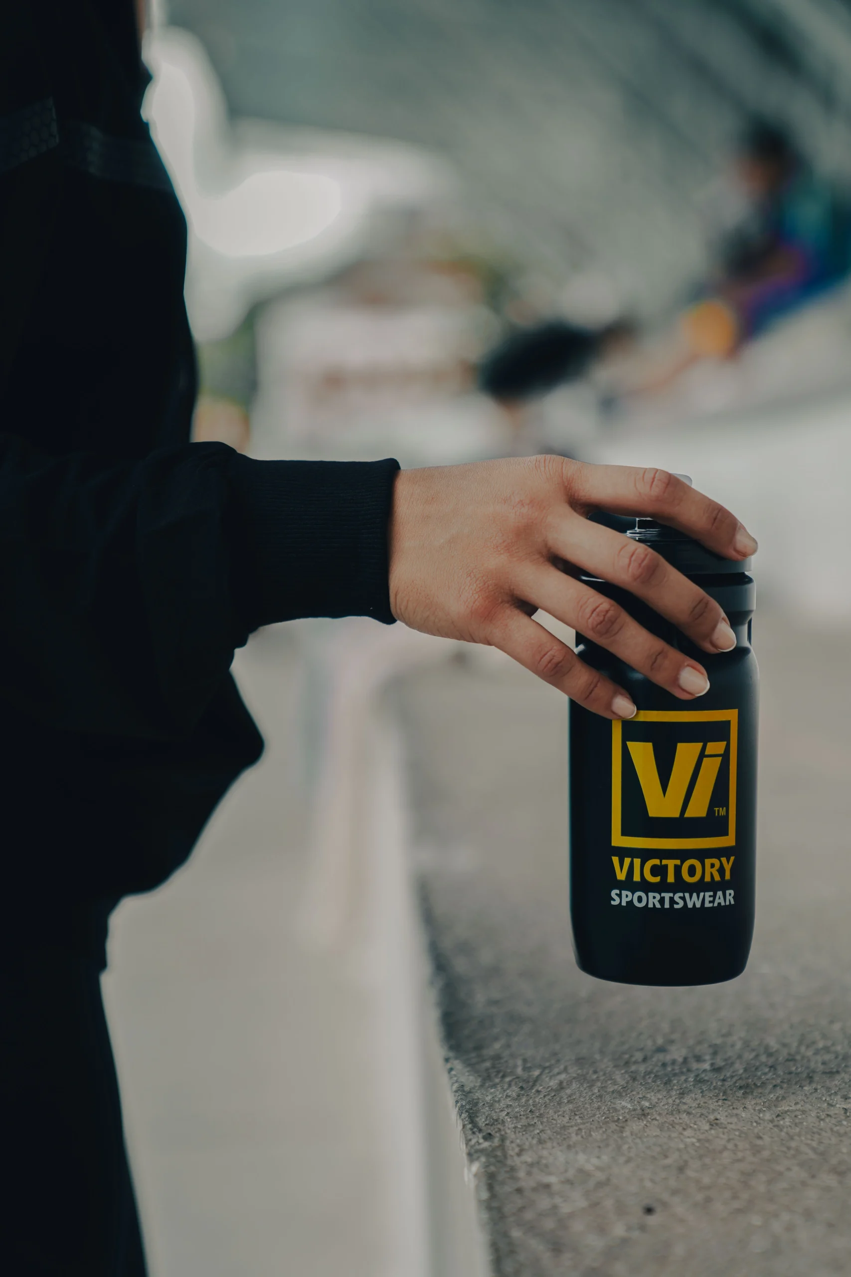 Mano sosteniendo botella deportiva negra con logotipo de Victory Sportswear – fotografía de producto minimalista por Suma Estudios