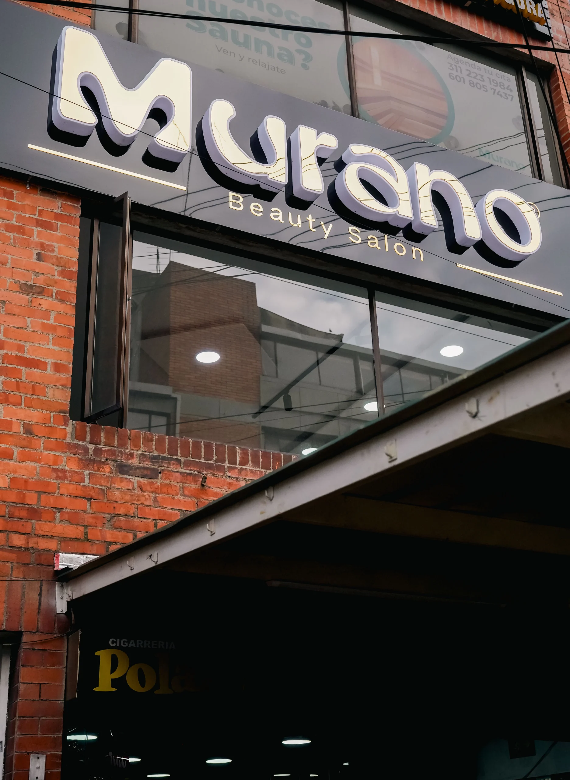 Letrero dorado en relieve de Murano Beauty Salon sobre fondo negro en fachada de ladrillo rojo – registro de identidad visual urbana por Suma Estudios