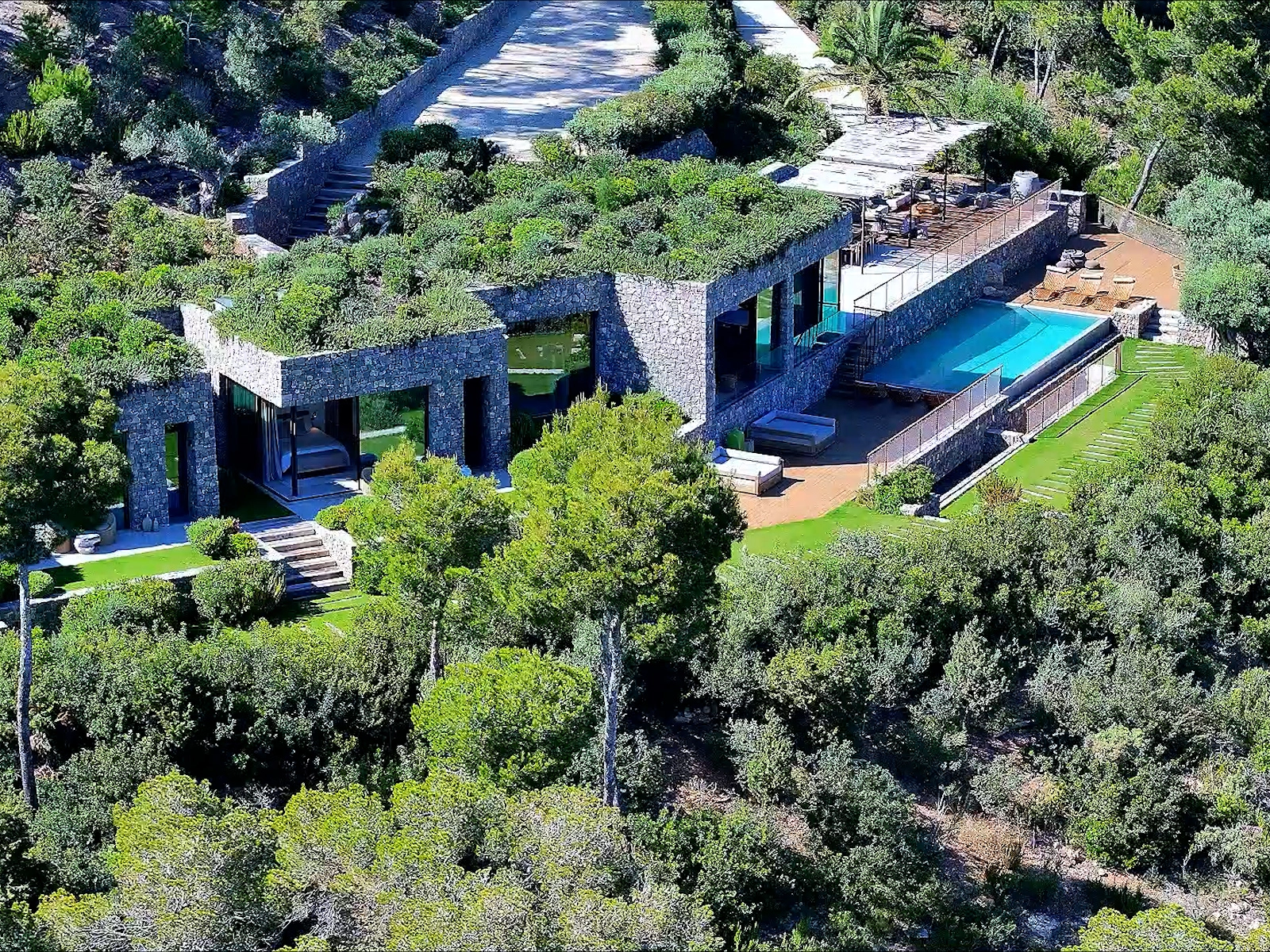 Residencia de lujo con arquitectura de piedra y techo verde, integrada al paisaje natural, fotografía contemplativa de piscina infinita – Suma Estudios.